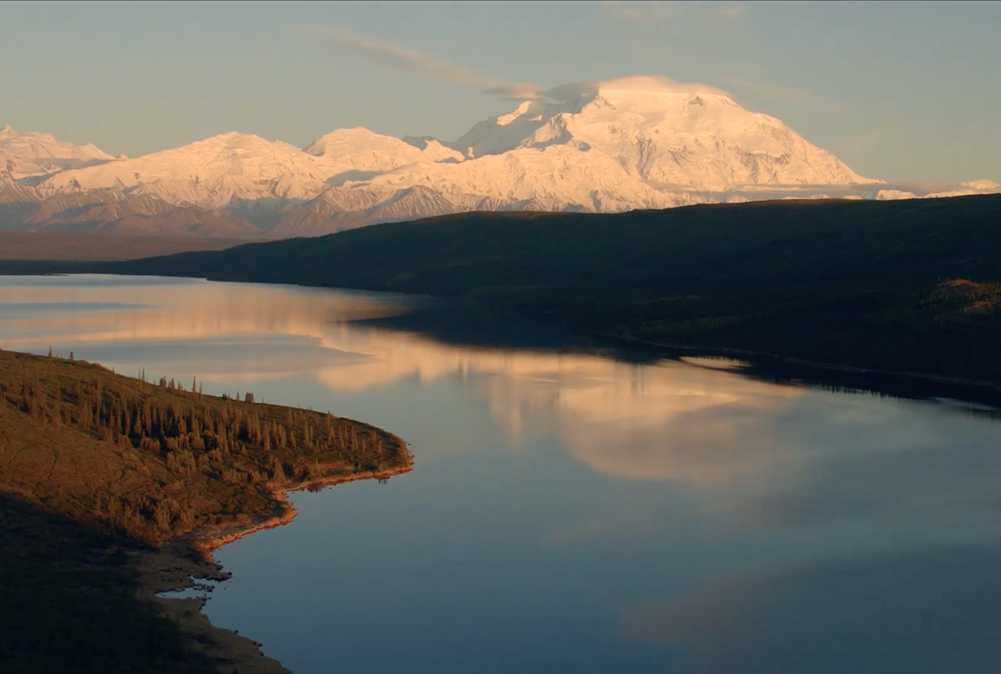Denali reflected in calm water at sunset in the Alaska Range