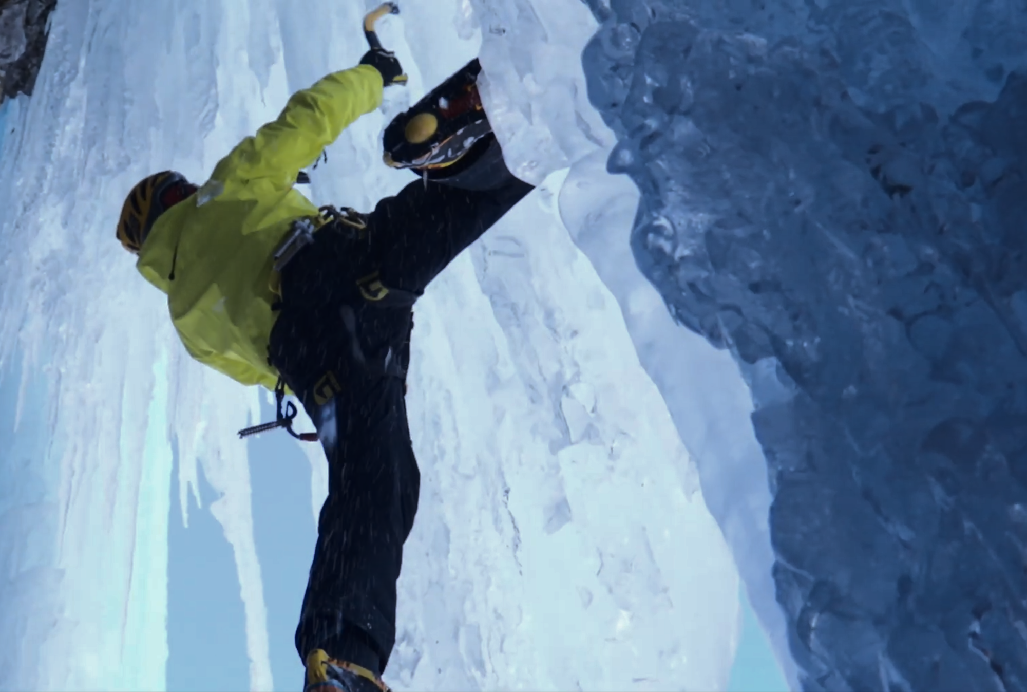 Ice climber ascending steep frozen terrain surrounded by ice formations and winter conditions.