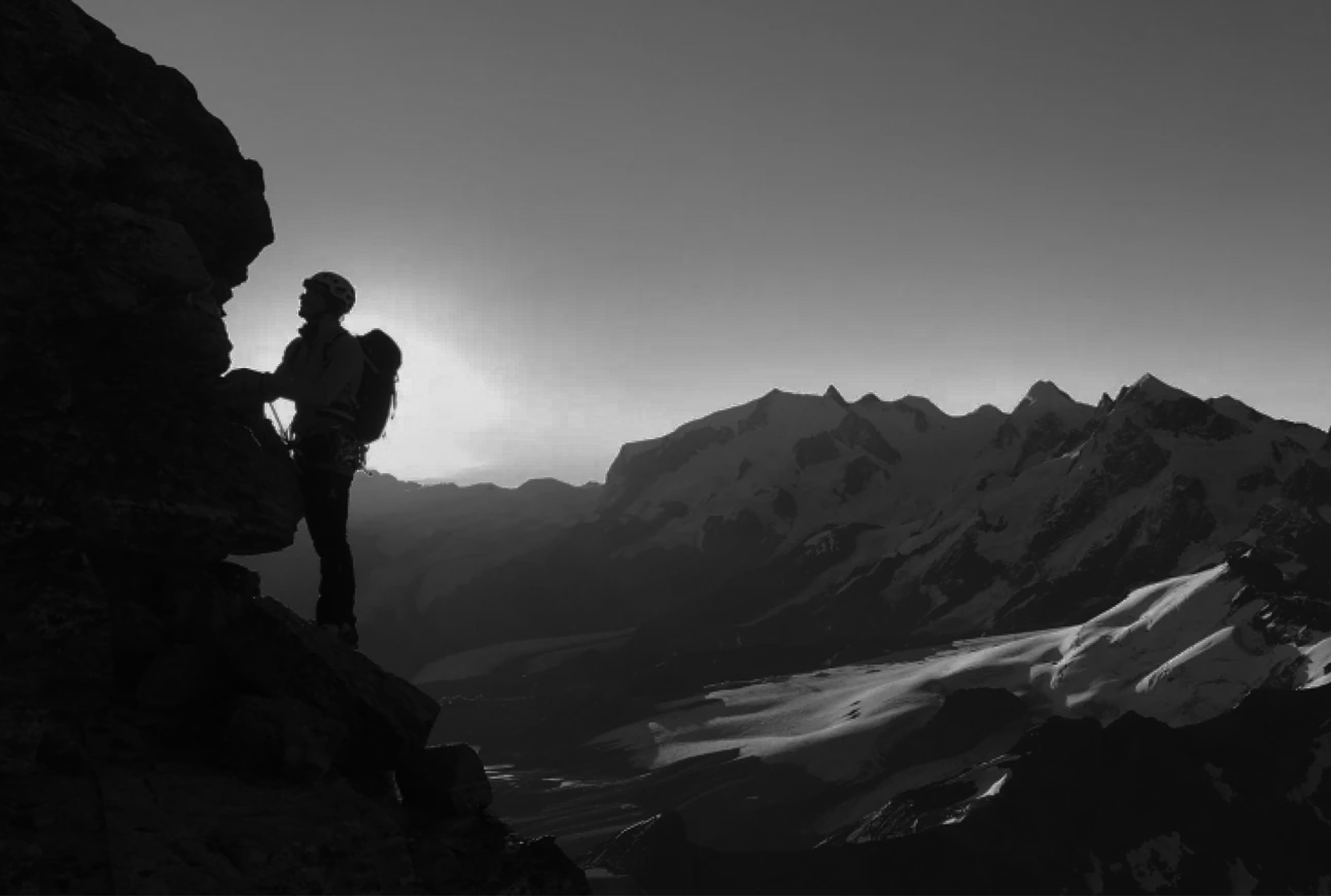 Silhouette of climber on rocky terrain at sunrise with alpine peaks and glaciers surrounding the Matterhorn.