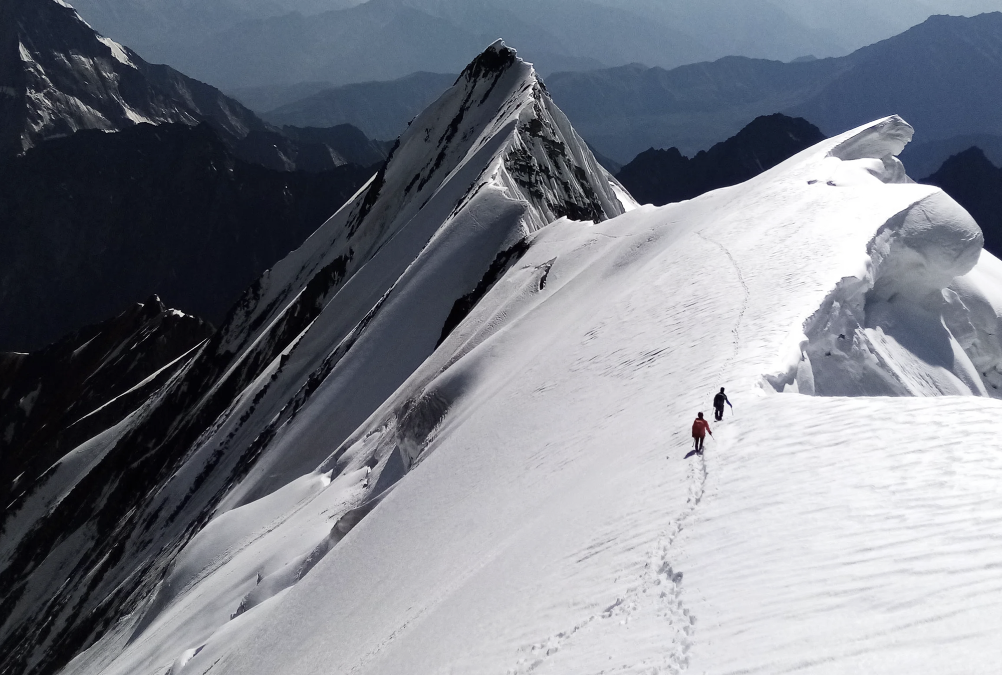 Helias Millerioux and Patrick Wagnon ascending a snow ridge above glaciated terrain in the Karakoram.