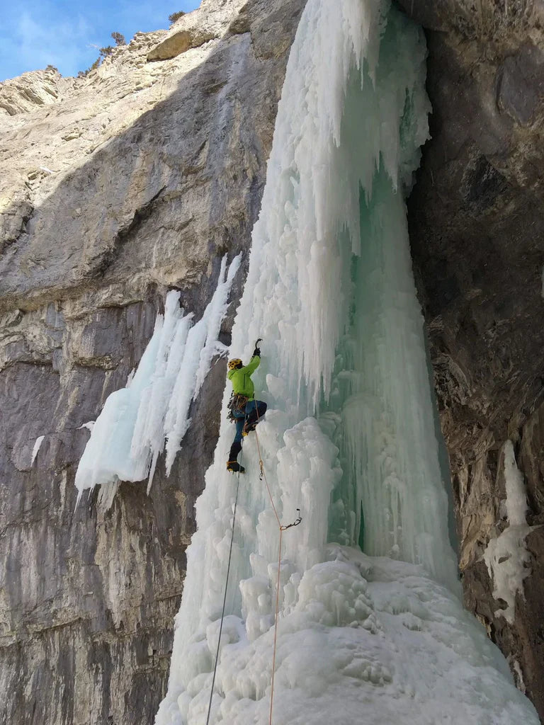 Ice climber ascending a wide blue frozen waterfall in Canada.