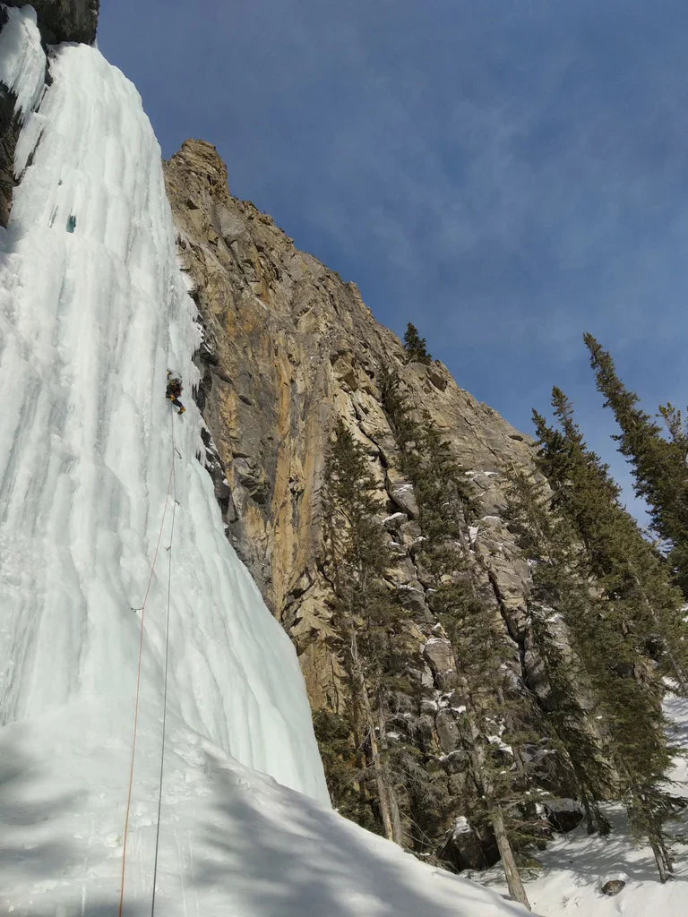 Climber on a tall frozen waterfall beside limestone walls and forest