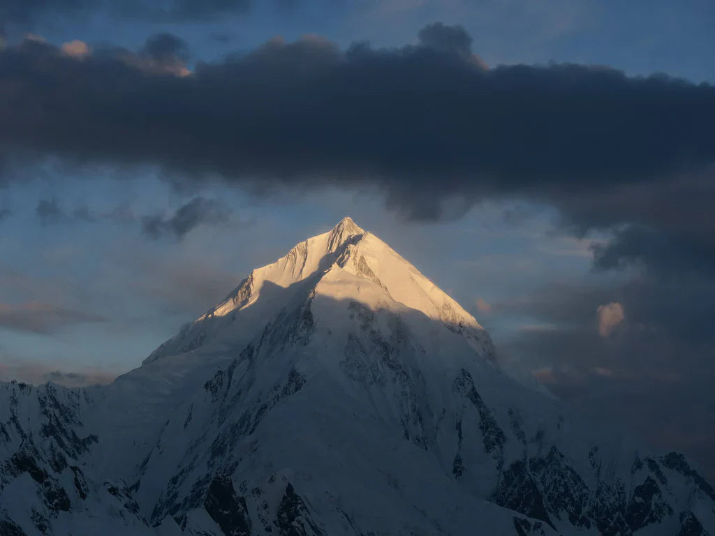 Sunlit snow summit beneath dark storm clouds in the Karakoram, Pakistan