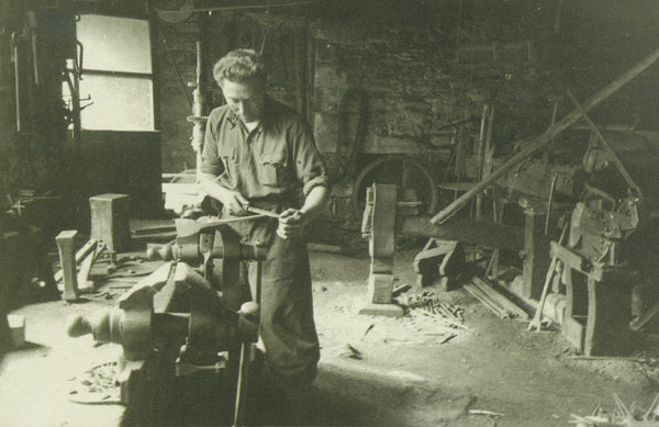 Historical blacksmith working on an ice axe inside the Grivel forge.