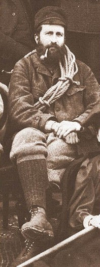 Portrait of Oscar Eckenstein seated with climbing rope and pipe.
