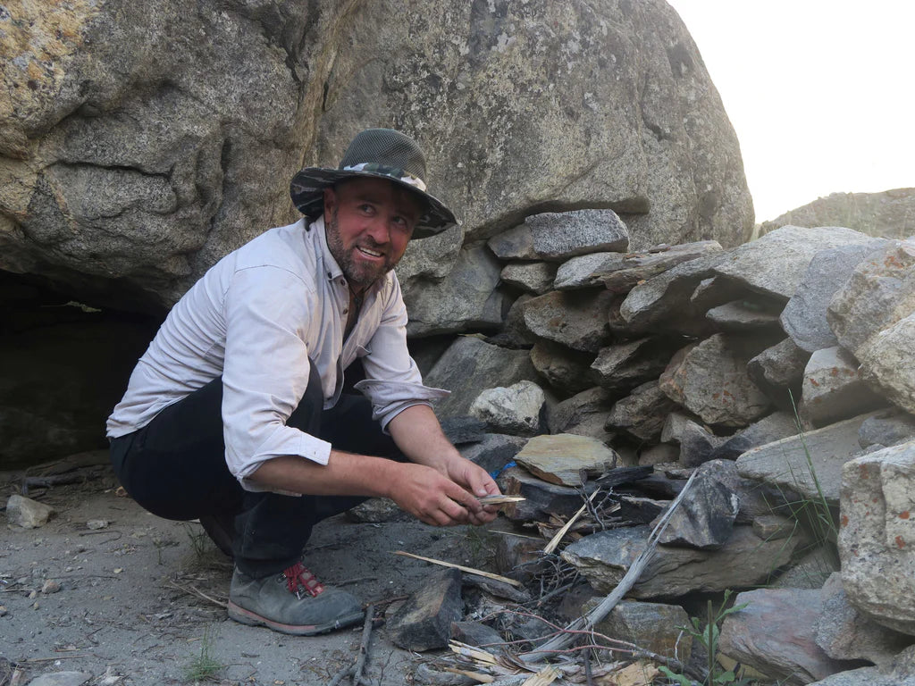 Expedition member preparing a fire beside granite boulders in Pakistan.