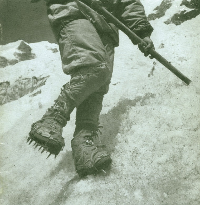 Early mountaineer ascending steep snow wearing original Grivel crampons.