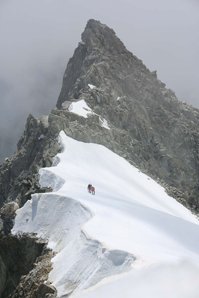 Climbers moving along a snow ridge beneath the Aiguille Blanche de Peuterey.