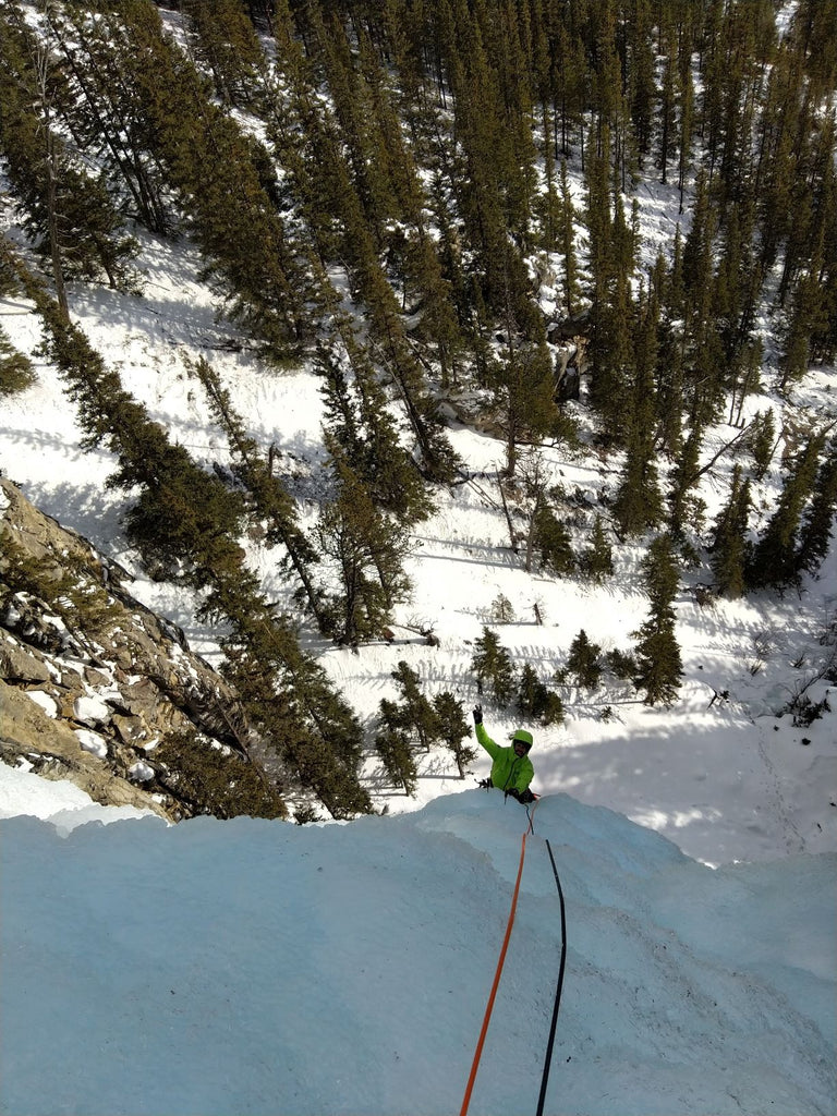 Climber belaying from the top of an icefall above a snowy forest