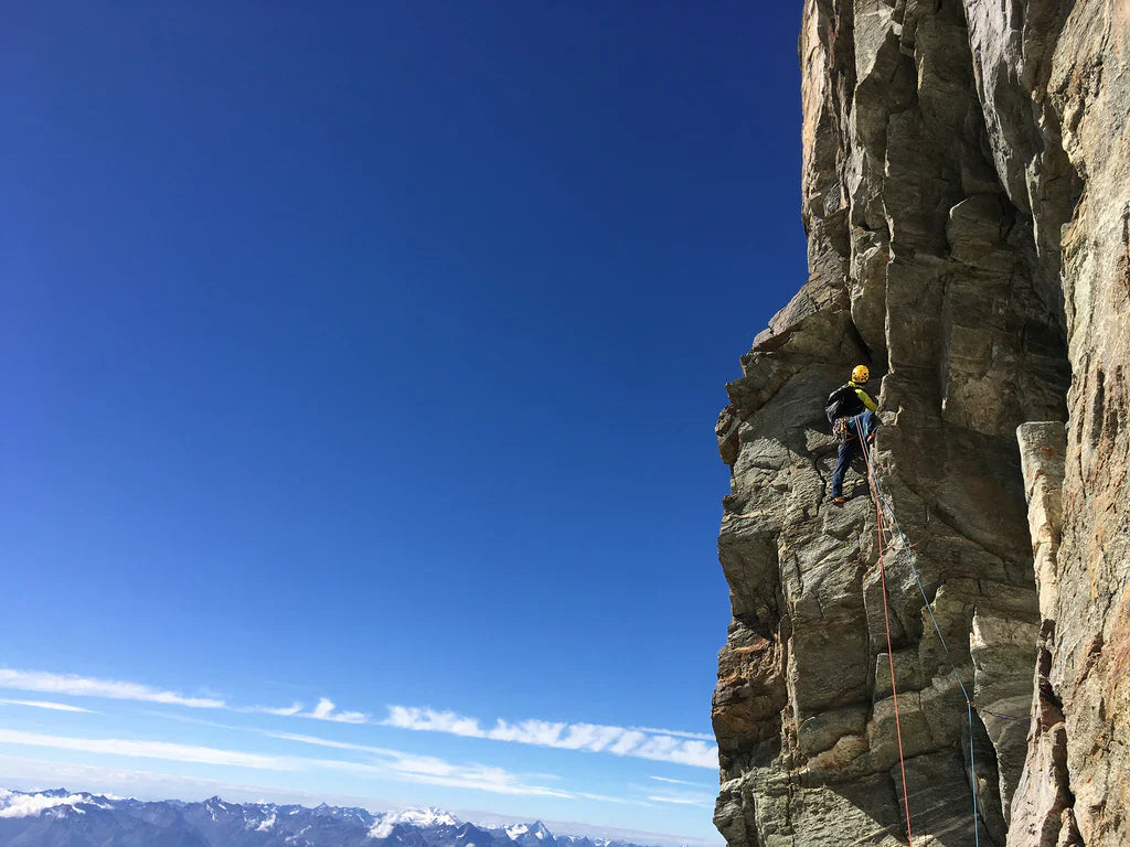 Jerome Perruquet ascending exposed rock terrain on the Matterhorn south face above the alpine valleys below.