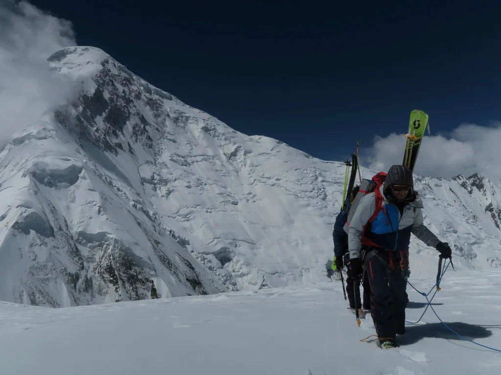 Expedition member crossing glaciated terrain beneath a steep Karakoram face.